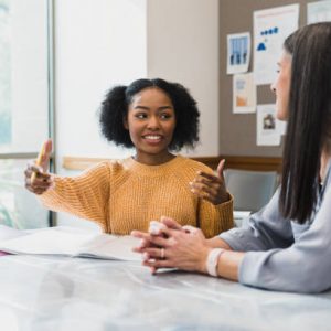 The teenage girl gestures as she explains something to her mid adult female teacher.